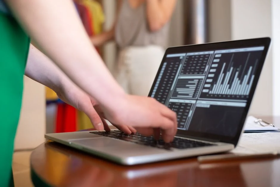 Person analyzes stock data with a smartphone and laptop, indoors.